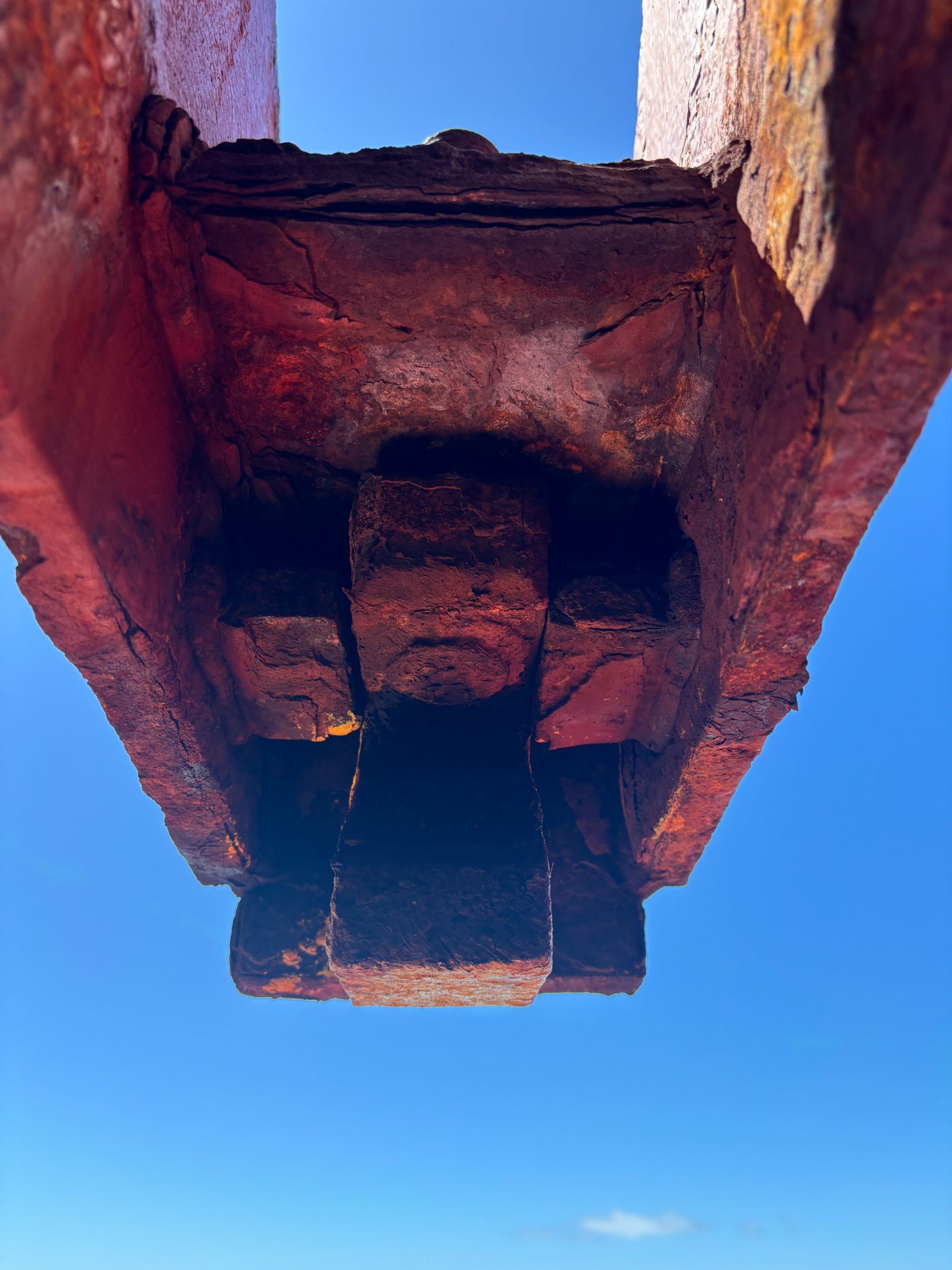 Severe corrosion and wastage on the underside of a structural member, seen from below against clear sky